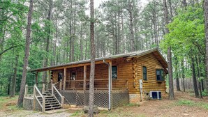 Une cabane rustique en rondins de bois, dotée d’un porche et d’un petit escalier menant à l’entrée.