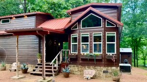 Une cabane en bois dotée d’un porche, de nombreuses fenêtres et de plantes en pot.