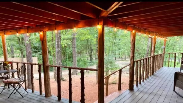 Une terrasse en bois avec une rambarde, des guirlandes lumineuses et une vue sur une forêt.