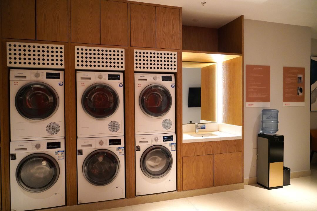 Un cuarto de lavandería con tres lavadoras apiladas, un lavamanos y un dispensador de agua.