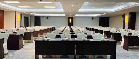 Une salle de conférence avec une longue table, des rangées de chaises et un projecteur fixé au plafond.