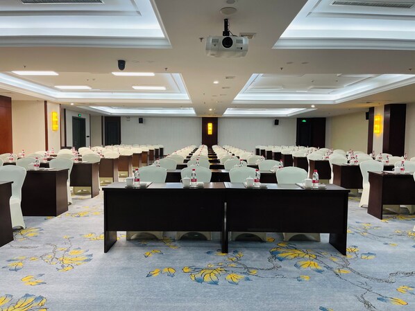 Une salle de conférence avec une longue table, des rangées de chaises et un projecteur fixé au plafond.