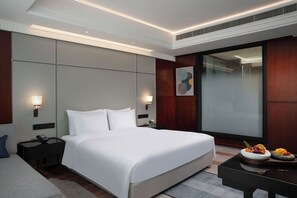 A modern hotel room with a large bed, bedside tables, a desk, and a dining area with fruit. - Yangzhou Wanda Yihua Hotel (Yangzhou)