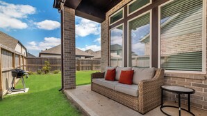 A patio with a wicker sofa, a small round table, and a grill.