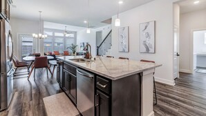 A modern kitchen with a large island, dark cabinetry, and pendant lighting.