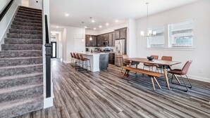 A spacious kitchen with modern appliances, a dining area with wooden tables and chairs, and a staircase with carpeted steps.