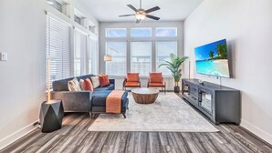 A modern living room with a sofa, two armchairs, a coffee table, and a TV on a wall.