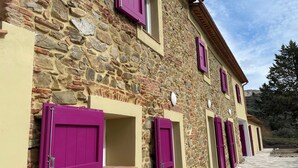 Un edificio de piedra con múltiples ventanas y puertas, algunas con contraventanas moradas.