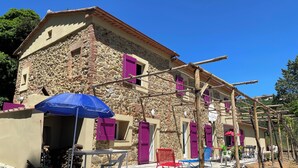 Un edificio de piedra con varias habitaciones, un patio con mobiliario exterior y una estructura de pérgola.