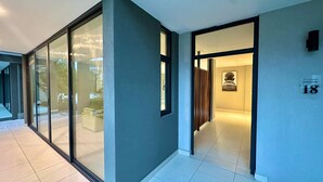 A modern hotel corridor with glass doors, a wooden partition, and a numbered room sign. - One Roma by Cubes (Lusaka)
