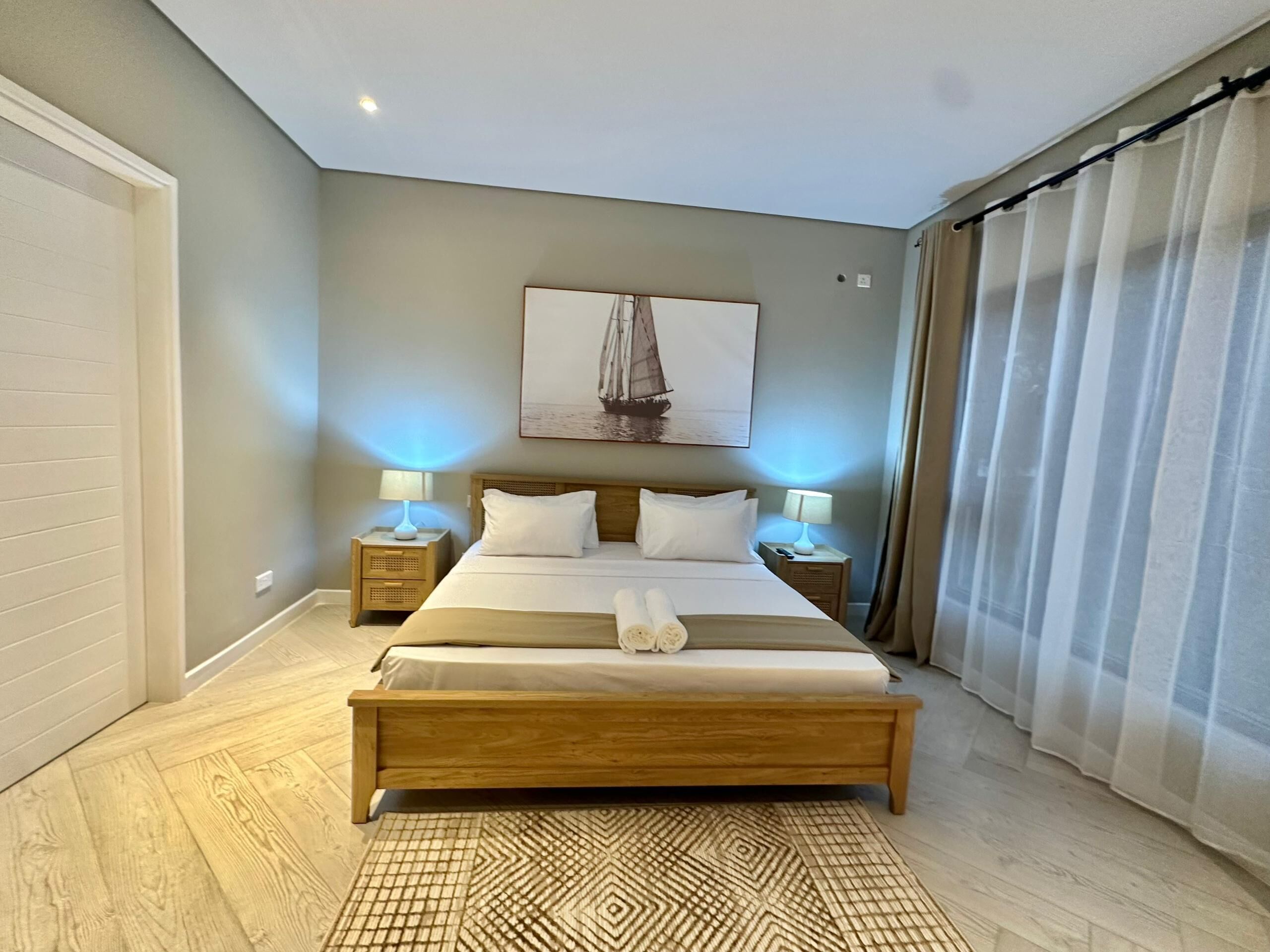 Une chambre à coucher avec un lit en bois, deux tables de chevet avec des lampes, un tapis à motifs et un tableau représentant un voilier accroché au mur.