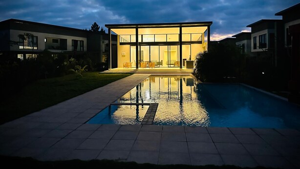 A modern house with a swimming pool in the foreground, large glass windows, and a well-maintained lawn. - One Roma by Cubes (Lusaka)