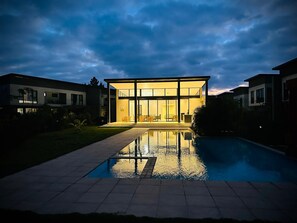 A modern house with a swimming pool in the foreground, large glass windows, and a well-maintained lawn. - One Roma by Cubes (Lusaka)