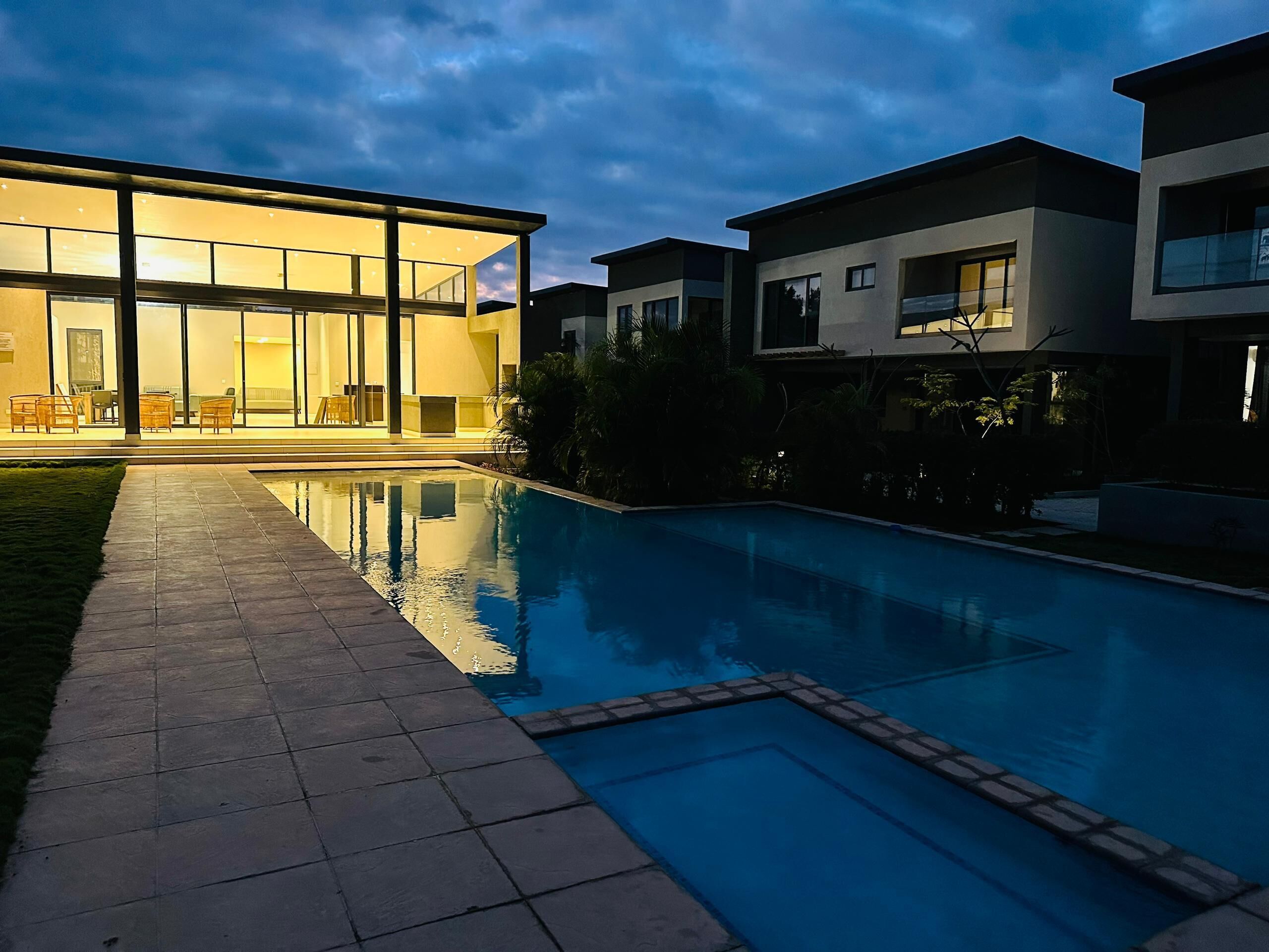 A modern residential building with a glass facade, a swimming pool, and a well-maintained lawn.