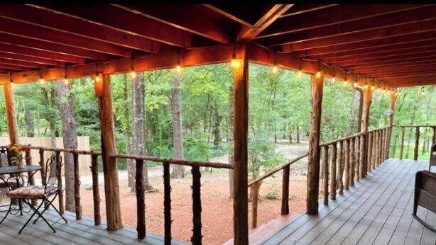 A wooden deck with a railing, a table with chairs, and string lights.