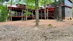 A cabin with a wooden deck and a covered area, surrounded by trees.