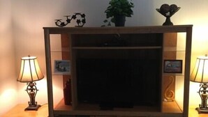 A living room with a wooden entertainment center, two lamps, a television, and a potted plant. - Calabay Parc - Spacious 4 bed to suit your family vacation (Davenport)