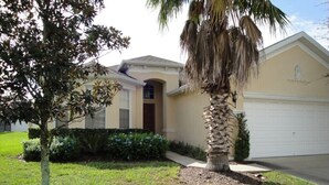 A single-story house with a garage, surrounded by a well-maintained lawn and a palm tree. - Calabay Parc - Spacious 4 bed to suit your family vacation (Davenport)