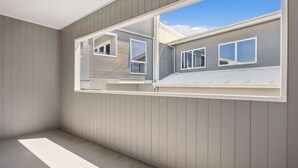A room with a large window, wooden walls, and a visible exterior view of a house. - Stratton Summit 2, 5 bedroom townhouse in Jindabyne. (Jindabyne)
