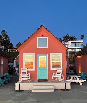 Un bâtiment rouge avec une porte turquoise, deux chaises berçantes blanches et une table de pique-nique.