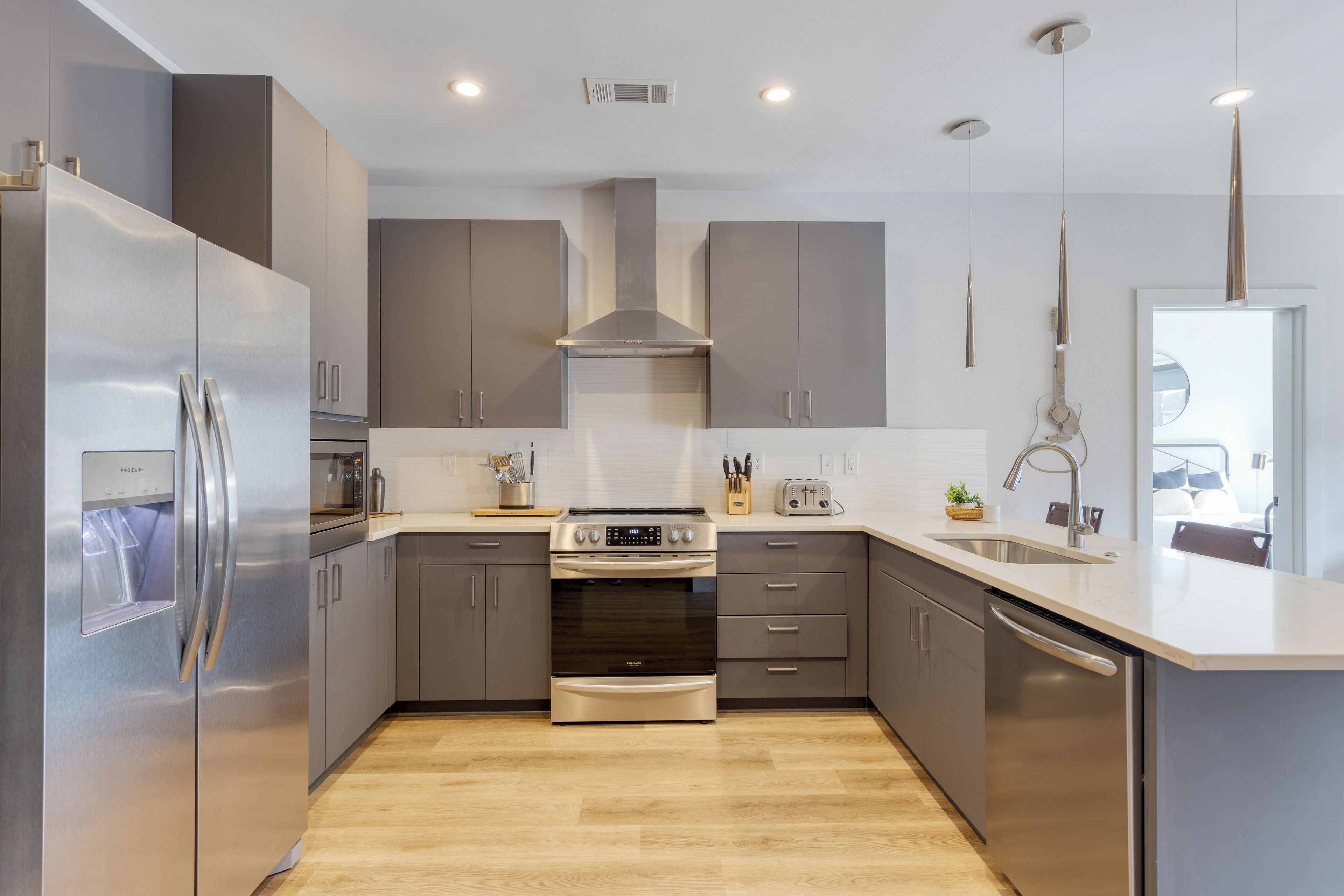 Une cuisine moderne dotée d’appareils électroménagers en acier inoxydable, de meubles de couleur grise et d’un plancher en bois.