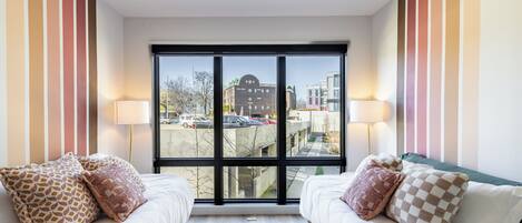 Ein Hotelzimmer mit zwei Betten, gestreiften Wänden, großen Fenstern und Blick auf die Stadt.