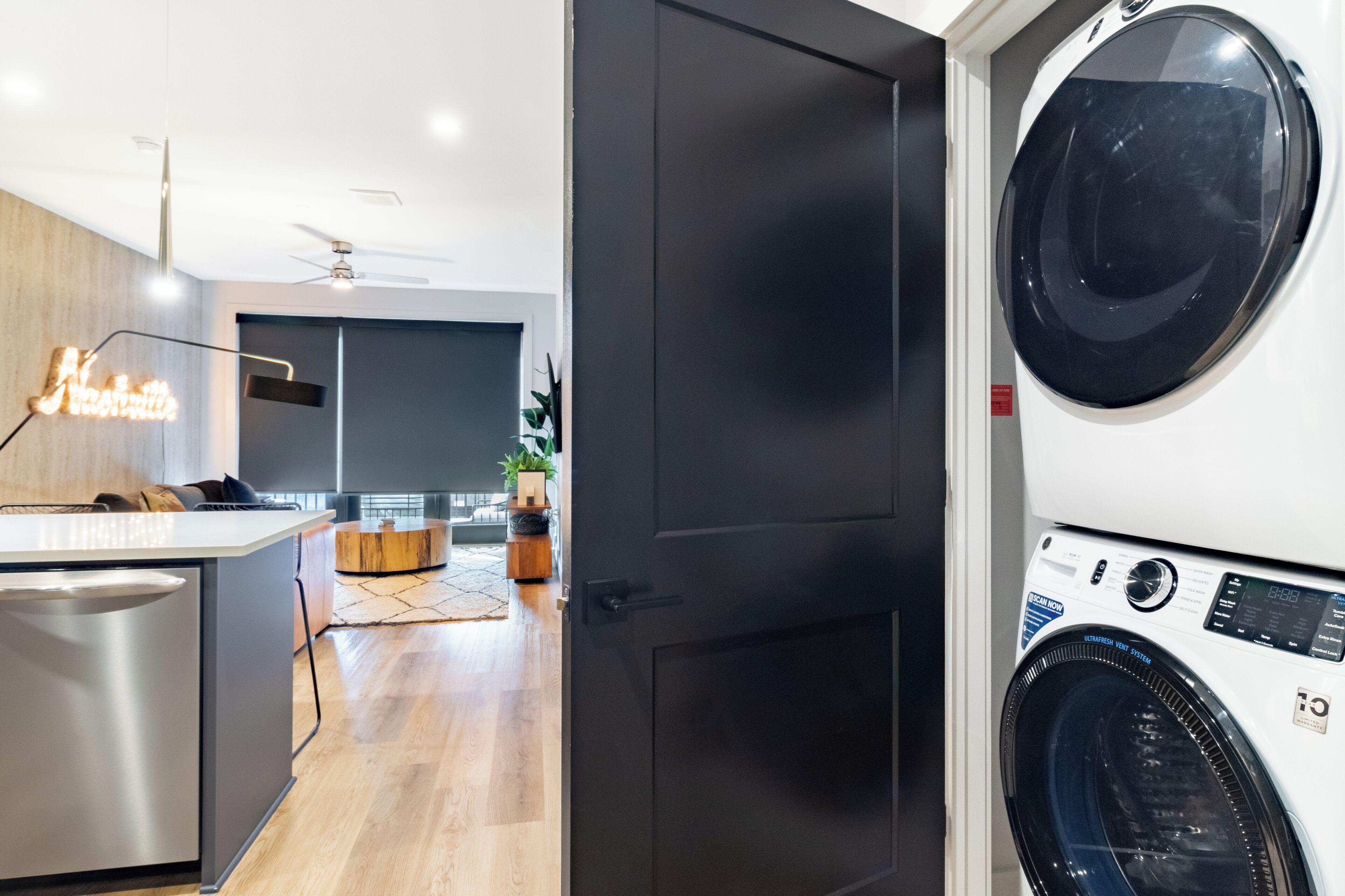 A modern laundry room with a front-loading washing machine and dryer, a wooden floor, and a neon sign.