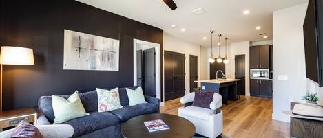 A modern living room with a sofa, armchairs, a coffee table, and a ceiling fan.