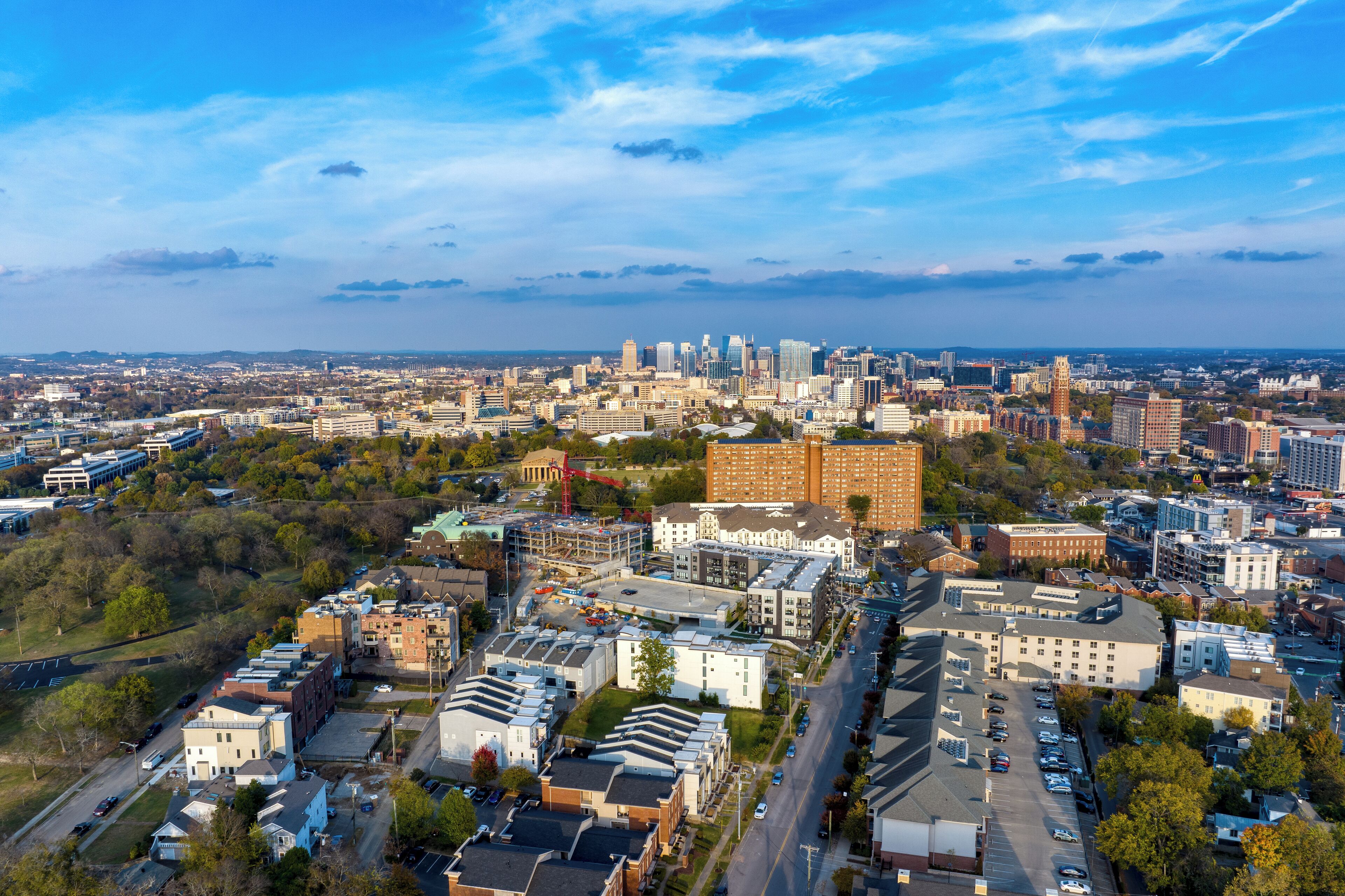 Une vue aérienne d’une ville, avec un mélange de bâtiments modernes et anciens, un ciel dégagé et une vue lointaine d’une ville plus grande.
