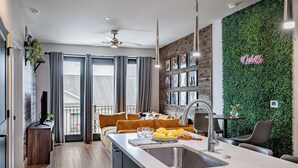A modern kitchen with a central island, a dining area with a sofa, and a green wall with a neon sign.