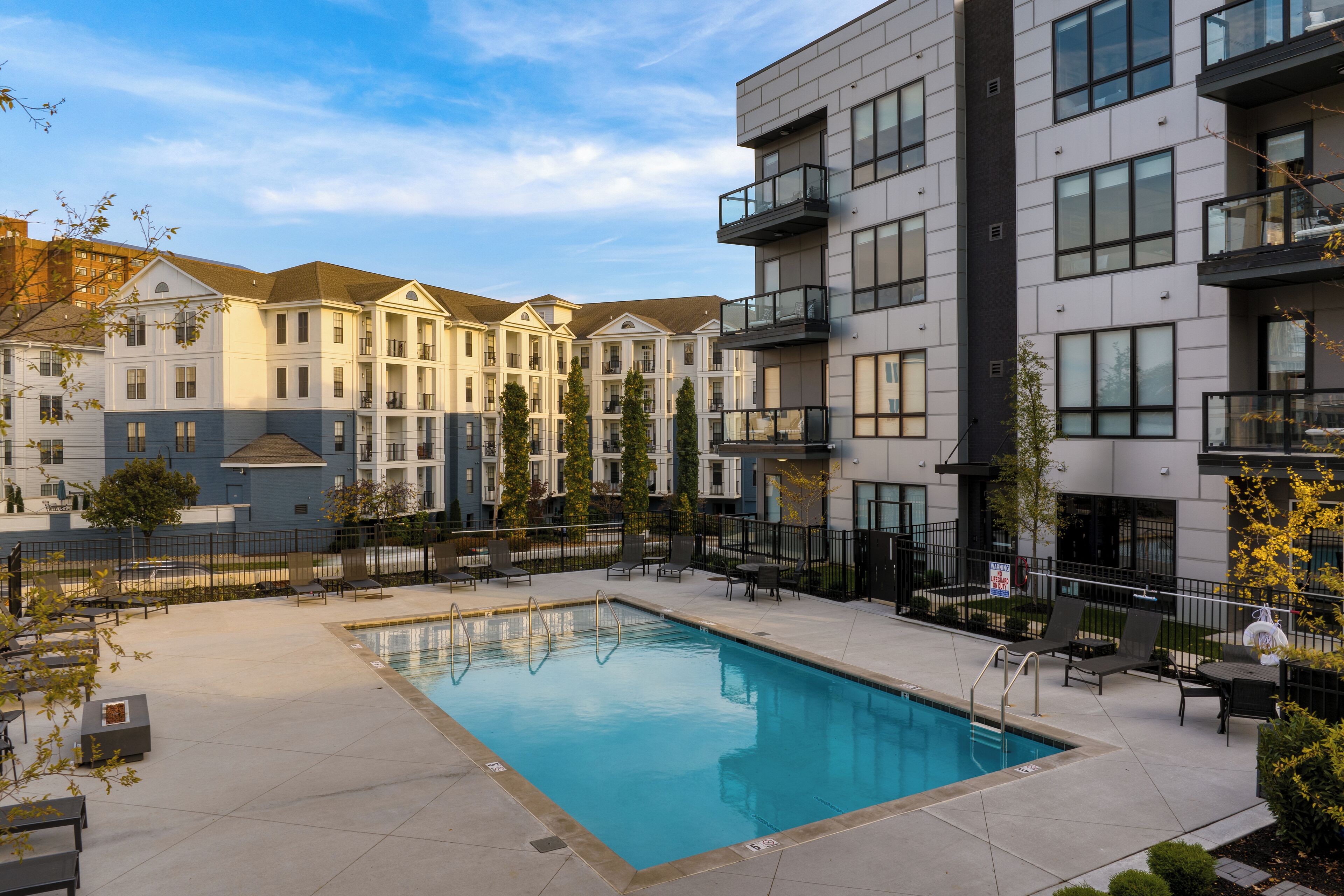 A modern apartment complex with a swimming pool, outdoor seating, and a mix of architectural styles.