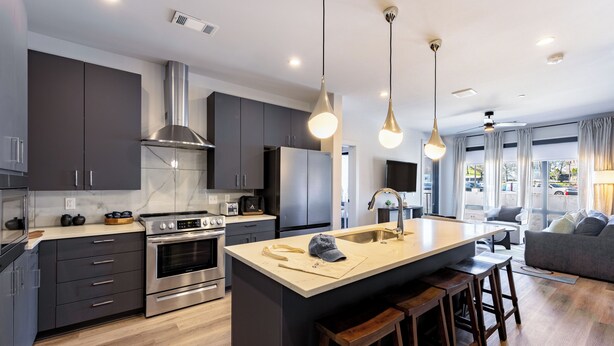 A modern kitchen with dark cabinets, stainless steel appliances, and a central island with stools.