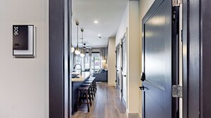 A modern kitchen with a long counter, pendant lights, and a view to the living area.
