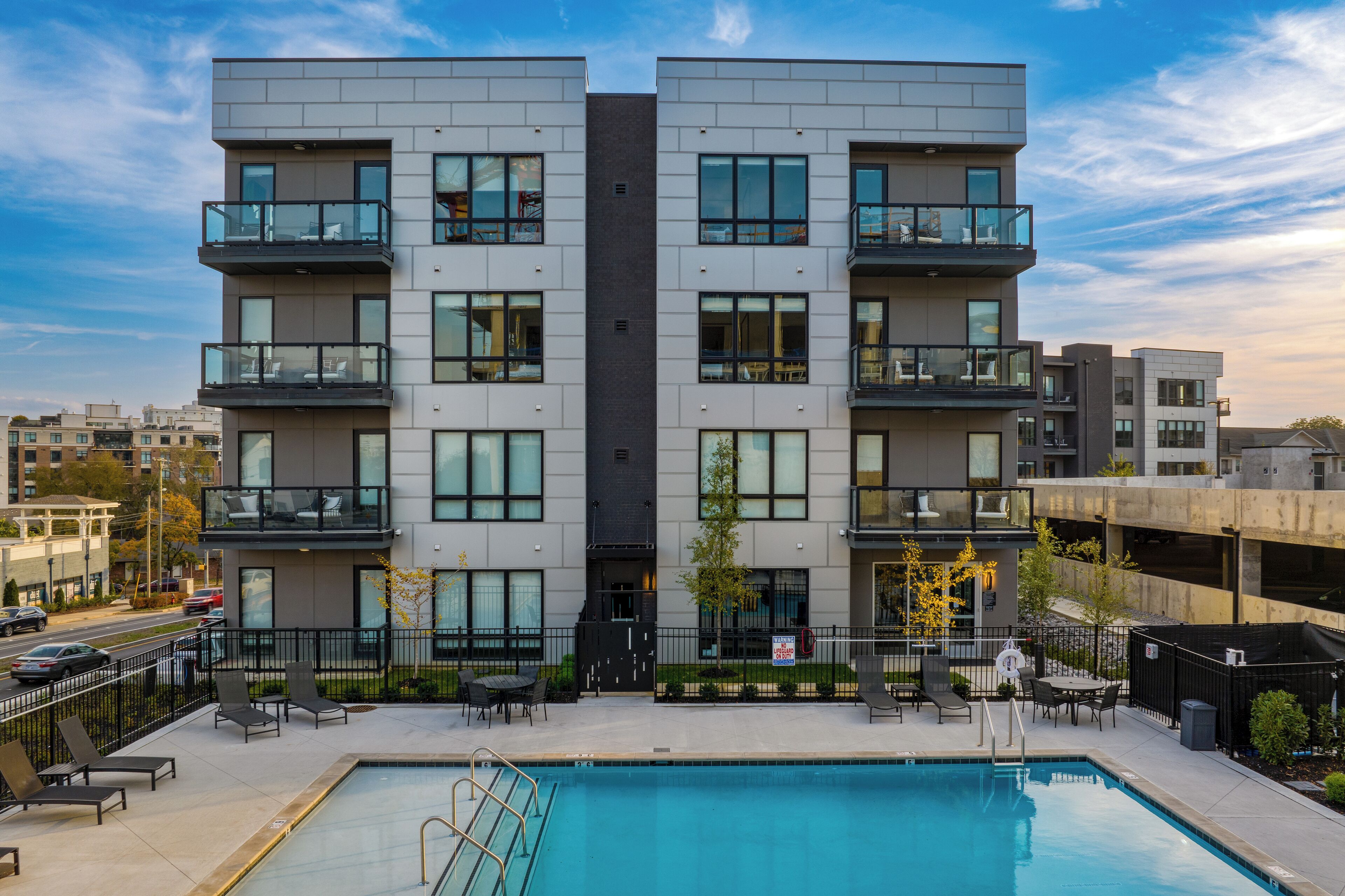 A modern multi-story building with balconies, a swimming pool, and outdoor seating.