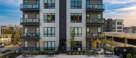Un edificio moderno de varios pisos con balcones, piscina y mobiliario de exterior.