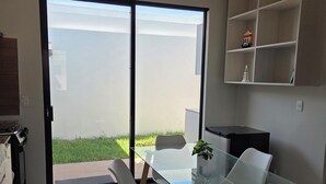 A modern kitchen with a glass dining table, white chairs, and a built-in shelf.