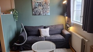 A cozy living room with a grey sofa, a small round table, a painting of a deer, and a window with curtains.