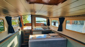 A cozy interior with a sofa, a small table, and a window overlooking water. - Unique nature experience on the water, Bed in boat Jisperveld (Spijkerboor)