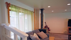 Una sala de estar con un sofá gris, una escalera con barandillas blancas, una chimenea y una guitarra.