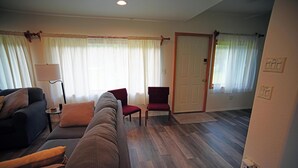 Una sala de estar con un sofá, sillones, una lámpara y una puerta que da a otra habitación.