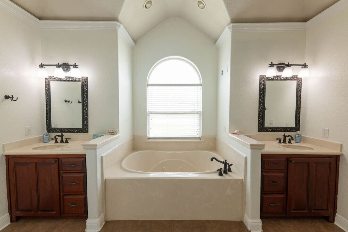 A bathroom with two sinks, a large bathtub, and a window with blinds.