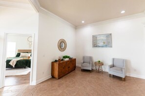 A spacious room with a wooden cabinet, two armchairs, a small round table, and a painting on the wall. - Lux Coastal Oasis | Pool • Hot Tub • Game Room (Biloxi)