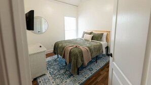 A bedroom with a bed, a bedside table, a mirror, and a ceiling fan.