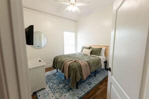 A bedroom with a bed, a bedside table, a mirror, and a ceiling fan. - Lux Coastal Oasis | Pool • Hot Tub • Game Room (Biloxi)