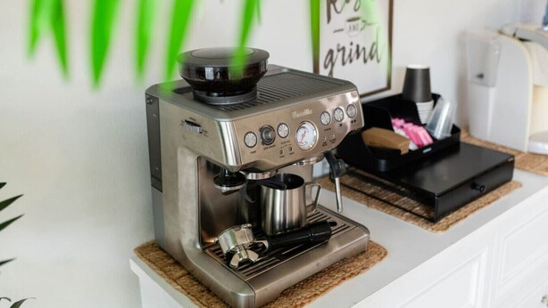 A coffee machine on a countertop with a coffee grinder and a framed sign in the background.