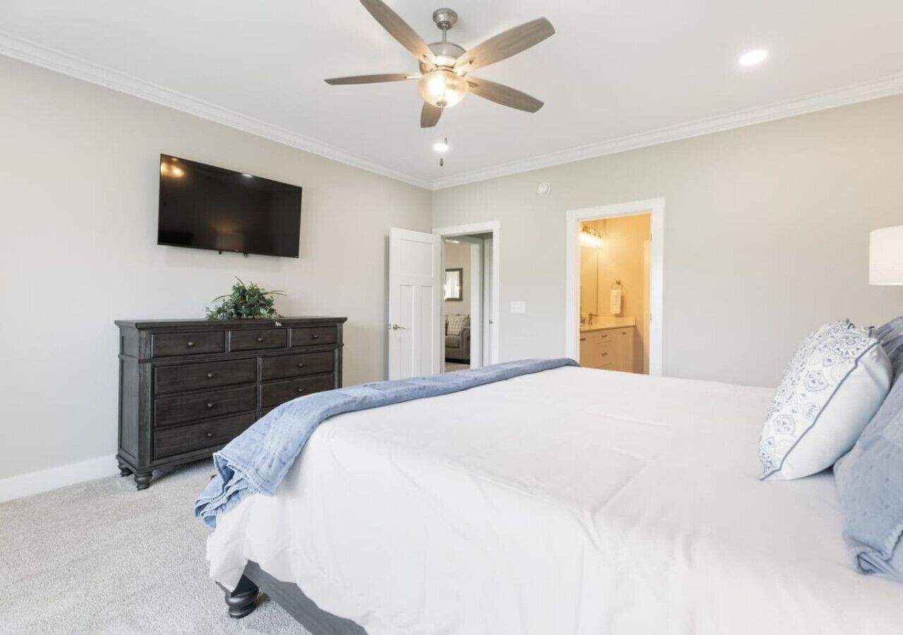 A bedroom with a bed, a dresser, a ceiling fan, and a TV mounted on the wall.