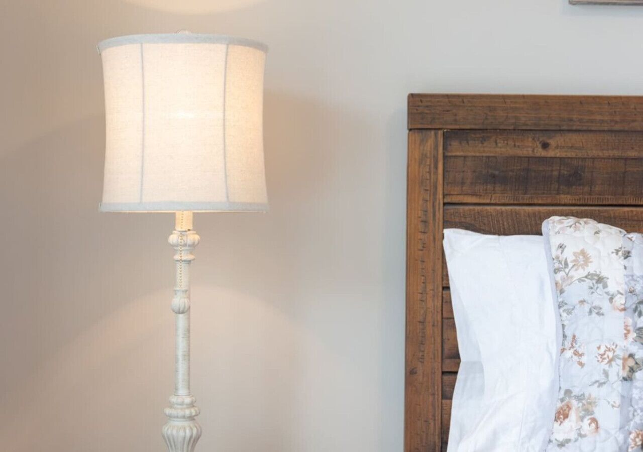 A bedside table with a lamp, a wooden headboard, and a floral pillow.