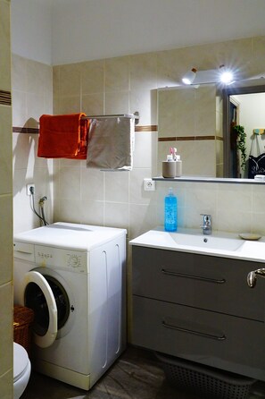 Une petite salle de bain équipée d’un lave-linge, d’un lavabo, d’un miroir et d’un porte-serviettes.