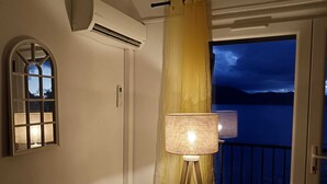 A room with a view of a lake at night, a window with a view of the sky, an air conditioning unit, and a lamp.