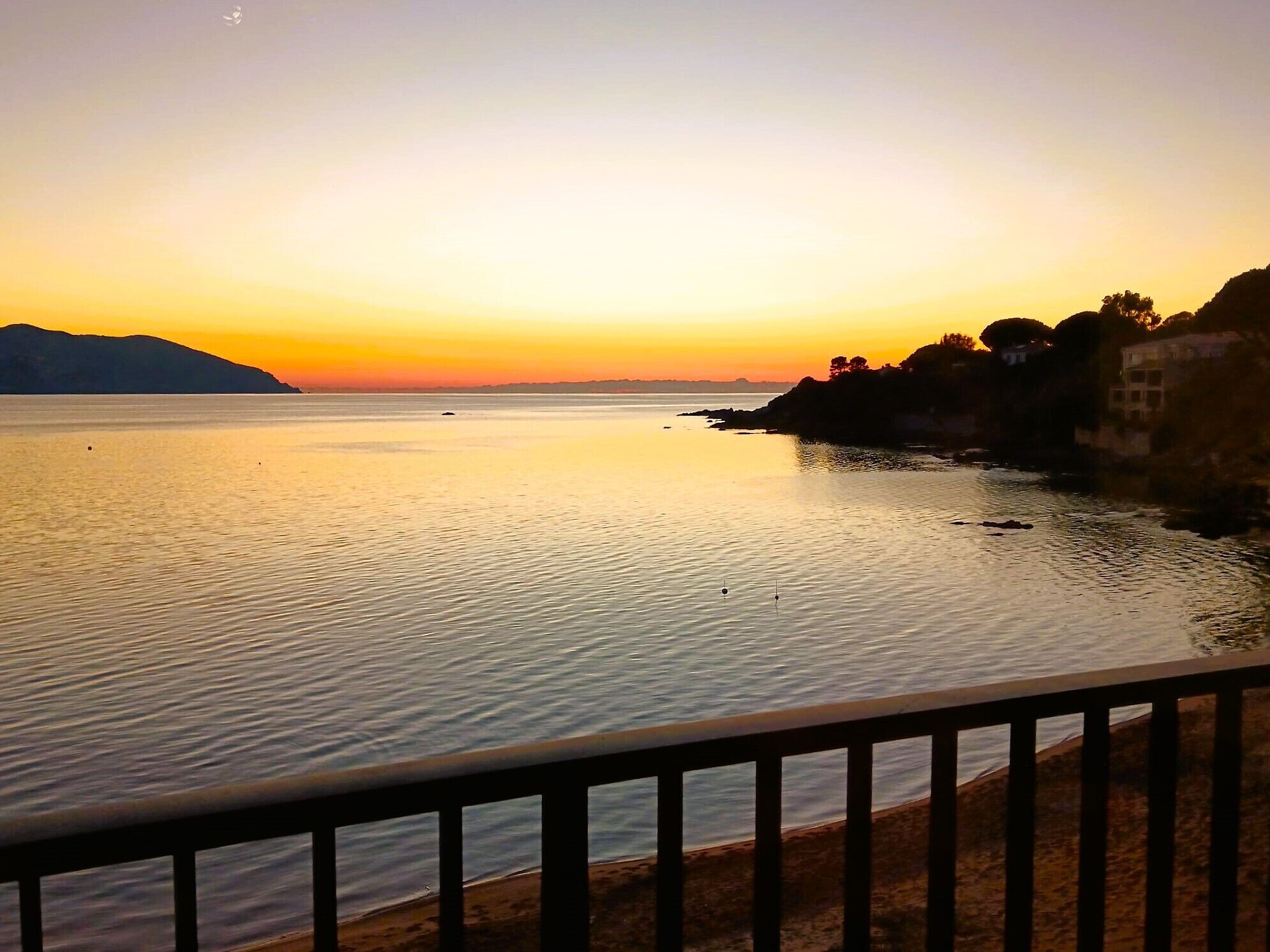 A calm body of water with a sunset, a distant mountain, and a building on the right.